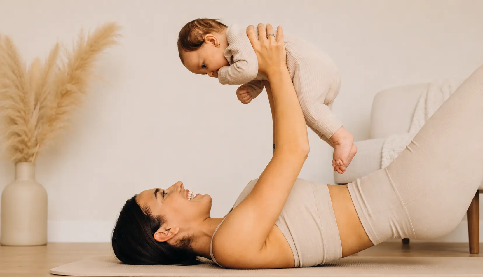 Une mère allongée sur un tapis tient son bébé au-dessus d’elle.